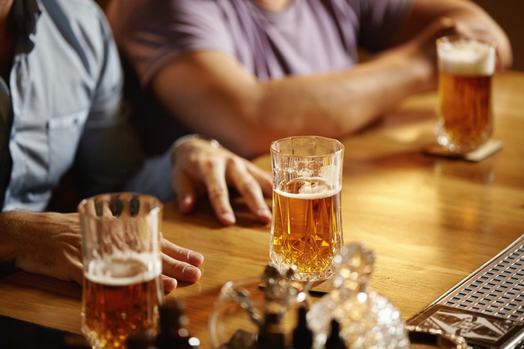 Friendly talk in club. Two happy young men chatting to each other while drinking lager or ale at bar